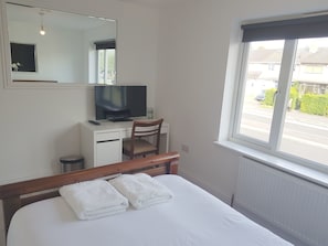 A bedroom with a bed, a desk with a computer and TV, a chair, and a window with a view of the street. - Oxford Modern Guest House (Oxford)
