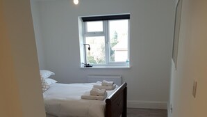 Un dormitorio con suelo de madera, una cama con ropa blanca, una ventana con vistas y un radiador.