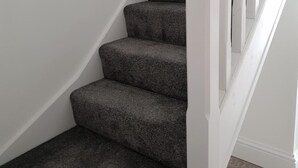 Una escalera con peldaños cubiertos de alfombra oscura y barandillas blancas.