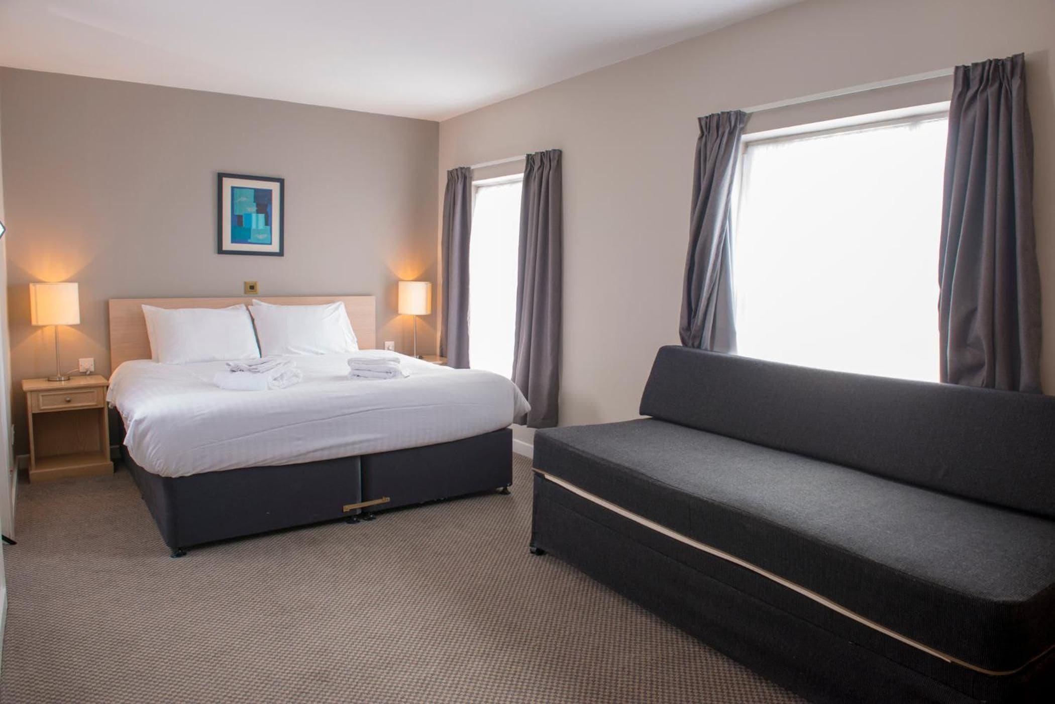 Een hotelkamer met een bed, nachtkastjes, een bank en een raam met gordijnen.