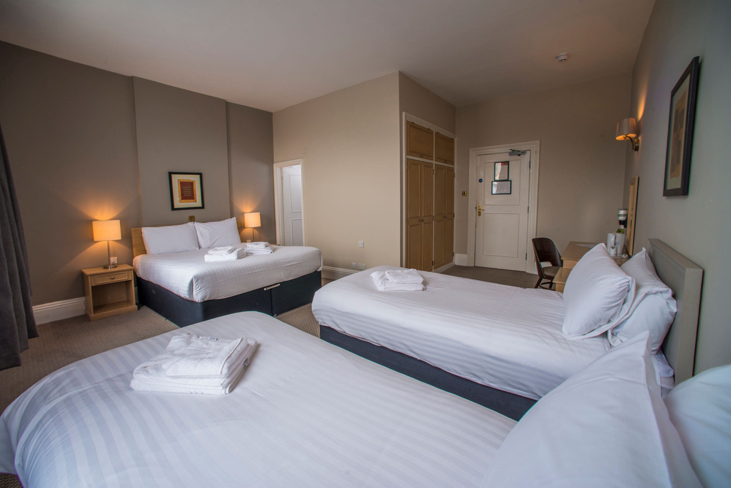 A hotel room with three beds, a desk, a chair, and a wardrobe.