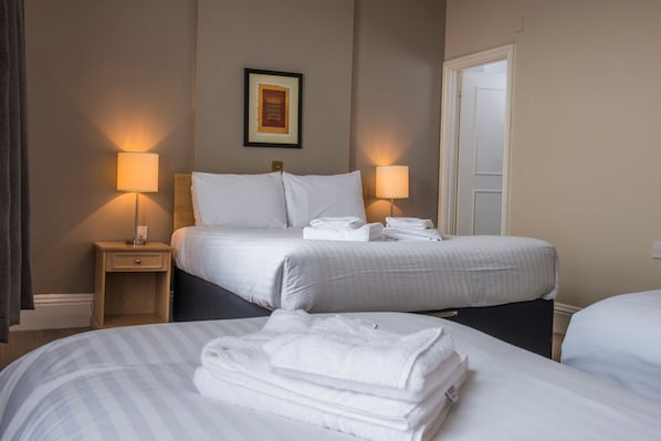 Quarto de hotel com duas camas, um quadro na parede e duas luminárias de cabeceira.