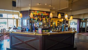 Eine Bar mit einer dunklen Holztheke, mehreren Lampen und einer Auswahl an Flaschen und Gläsern auf Regalen.