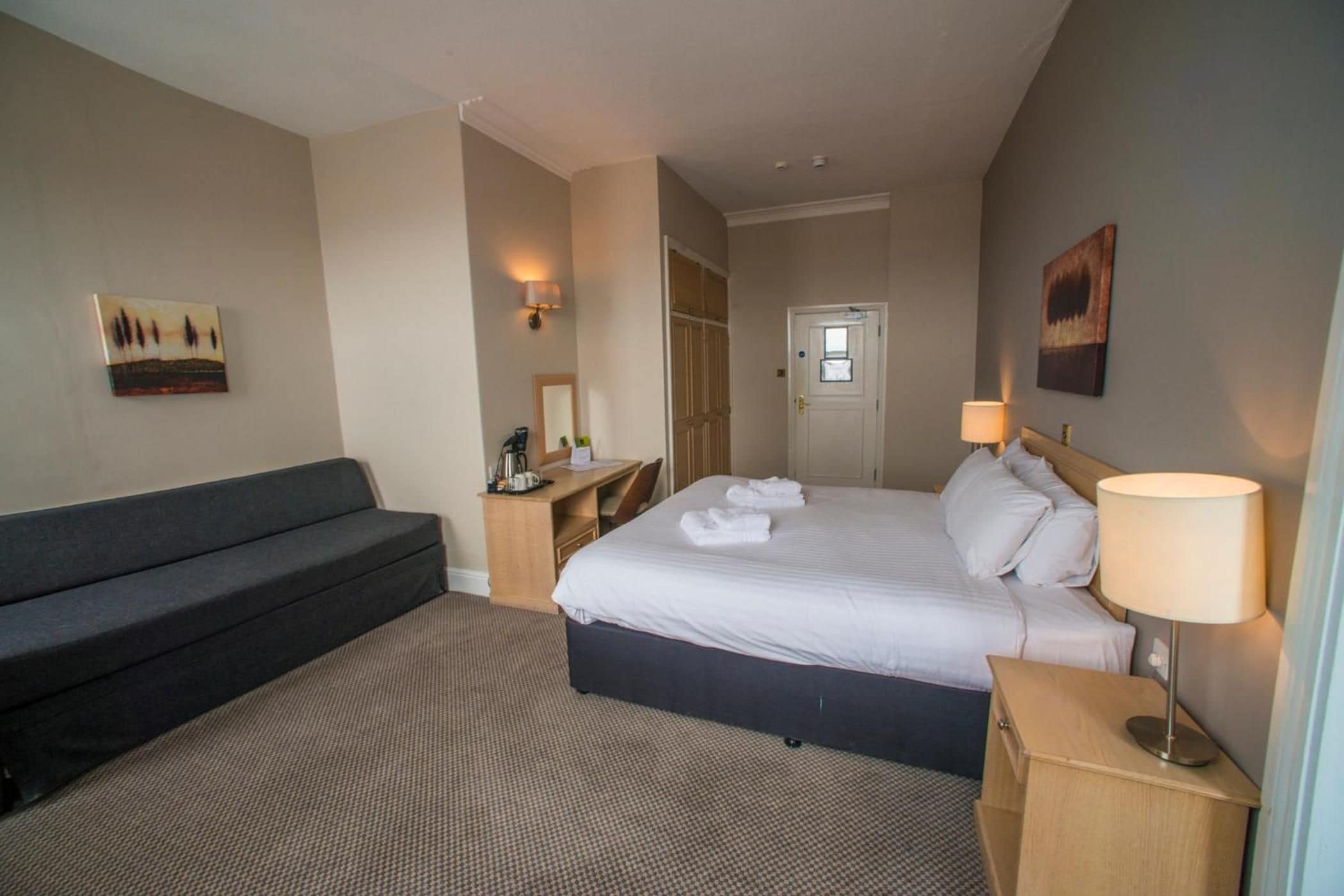Una habitación de hotel con cama, sofá, escritorio y lámpara.