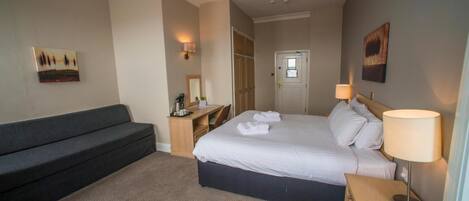 Una habitación de hotel con cama, sofá, escritorio y lámpara.