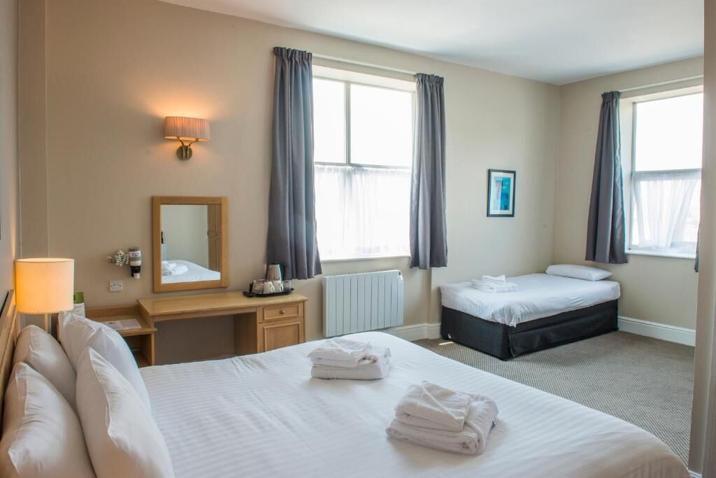 A hotel room with two beds, a desk with a lamp, a mirror, and a radiator.