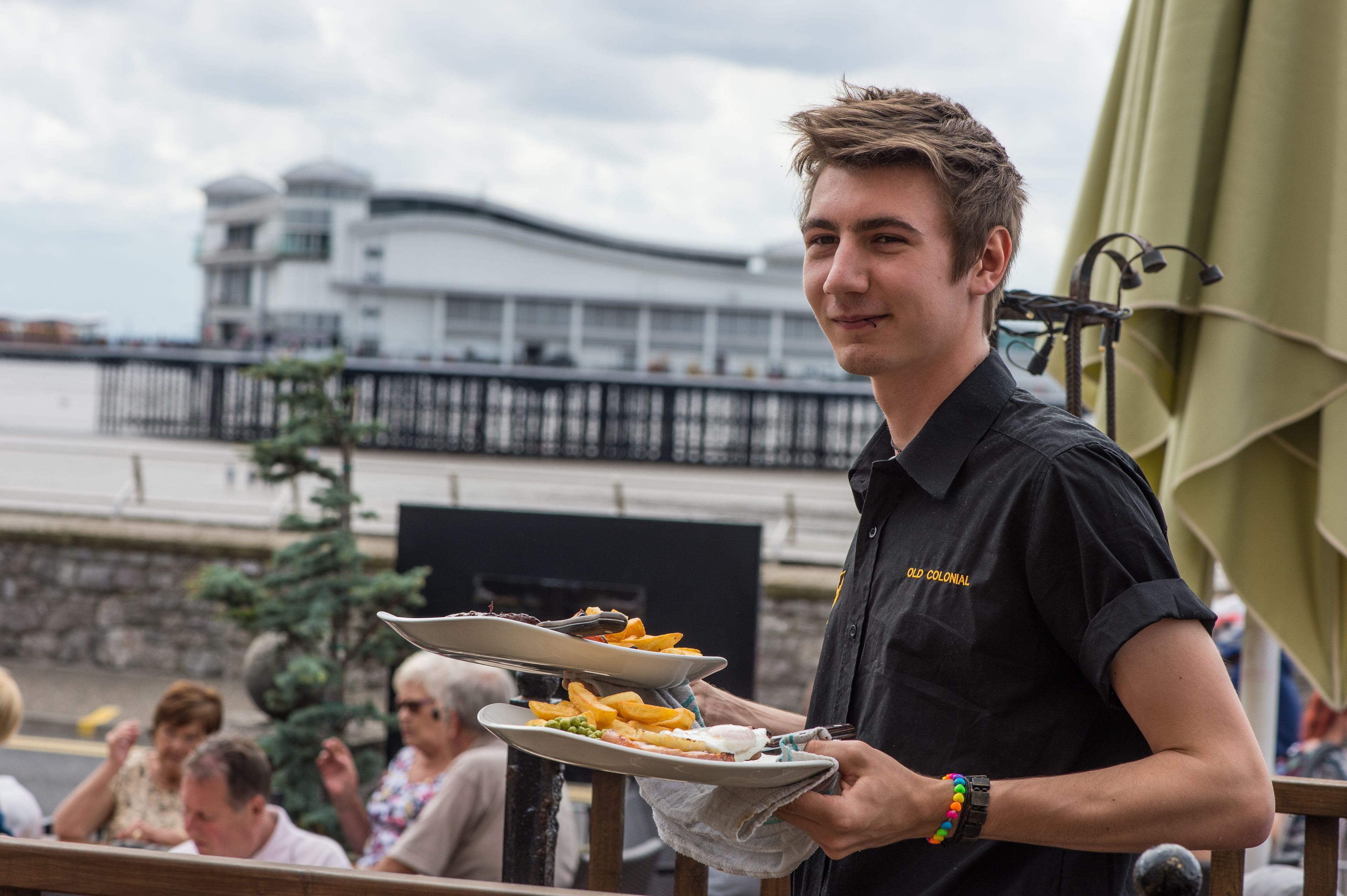 Eine Person serviert Essen im Freien, mit einem Gebäude im Hintergrund.