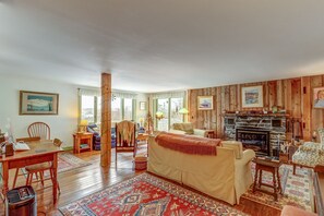 Cozy living room with a stone fireplace, dining area, and large window offering a view of the outdoors.