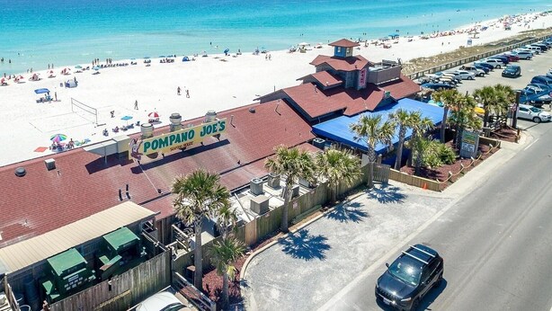 Un bien immobilier situé en bord de mer, avec une enseigne bien visible indiquant la présence d’un restaurant de fruits de mer, un espace de stationnement et une vue sur la plage.
