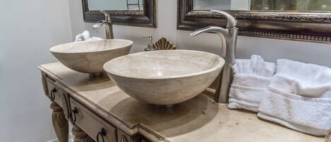A bathroom with two large, beige, bowl-shaped sinks, a vanity with ornate carvings, and a mirror with an ornate frame.
