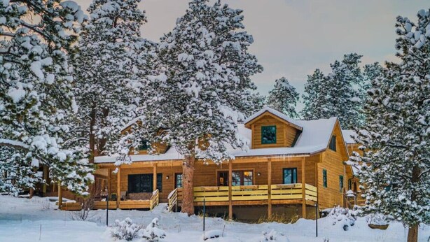 Une cabane en bois dotée d’un porche, entourée d’arbres couverts de neige.