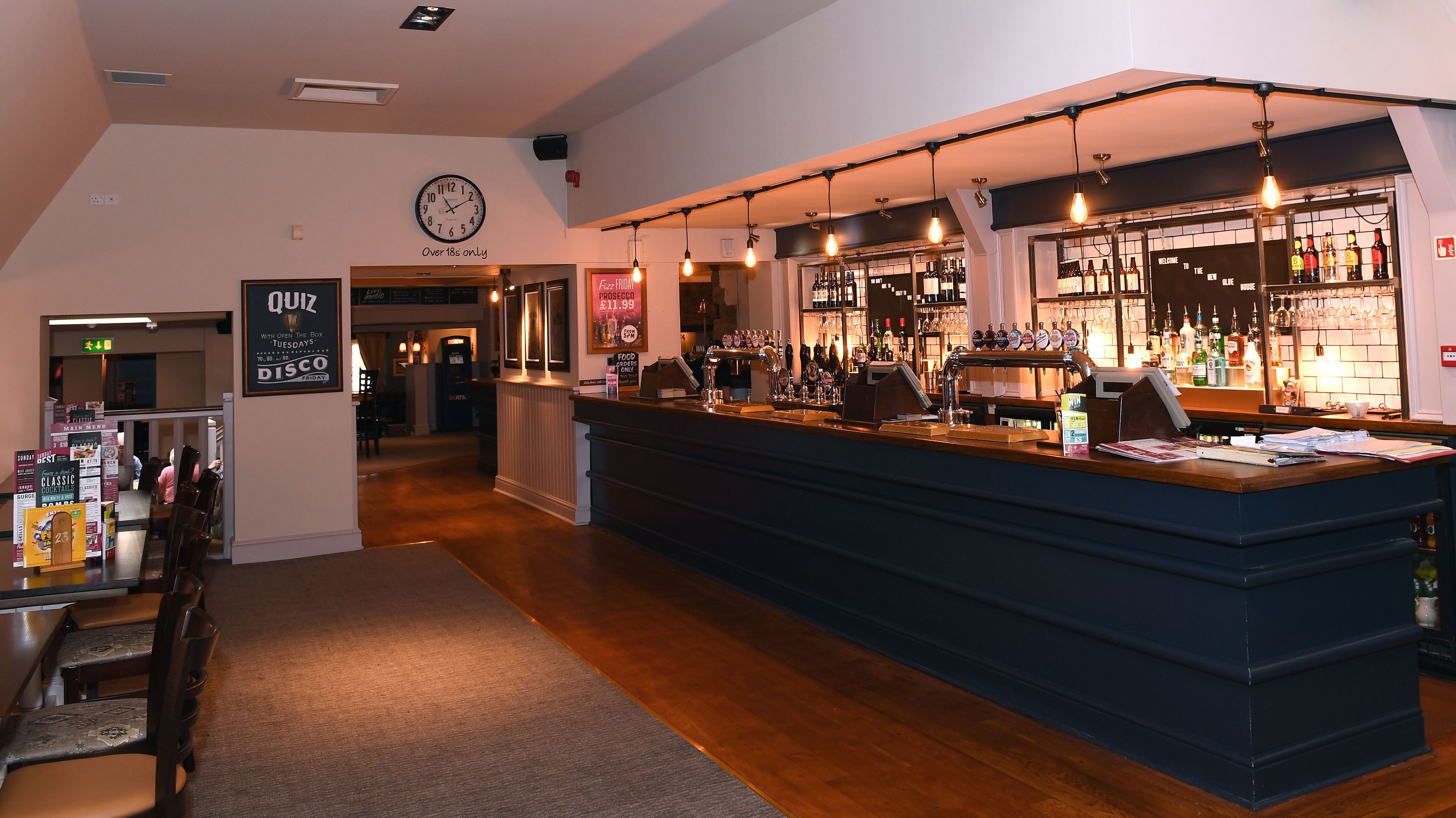 A bar area with a counter, shelves of bottles, and a clock on the wall.