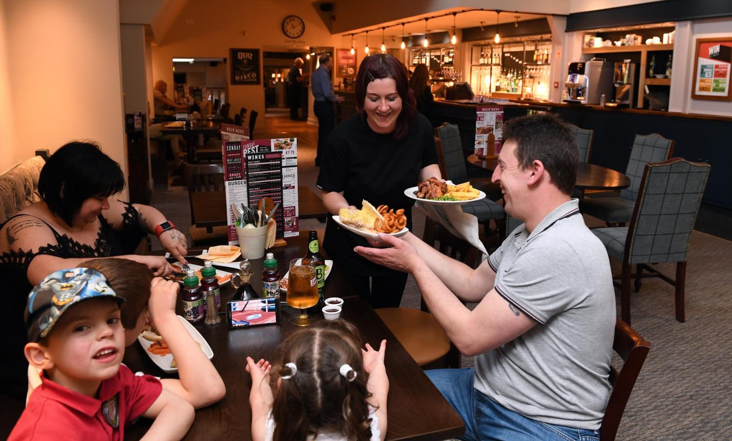 A family dining at a restaurant with a menu board, bar, and casual seating.
