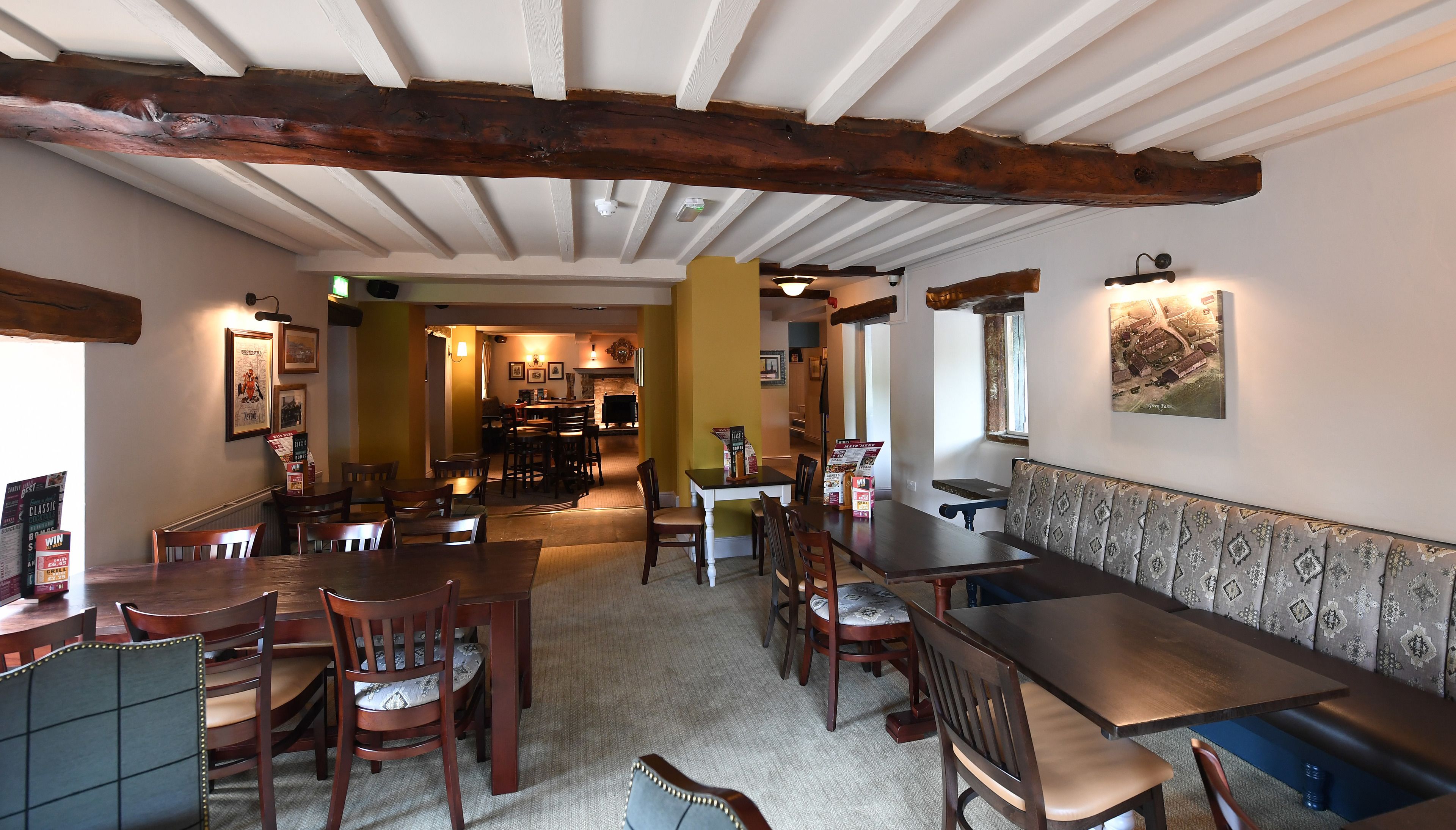 Een restaurant met houten balken, een lange toonbank en meerdere tafels en stoelen.