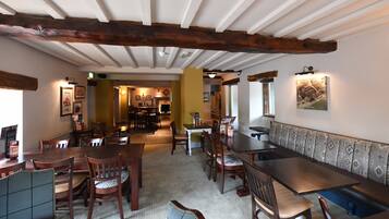 Een restaurant met houten balken, een lange toonbank en meerdere tafels en stoelen.