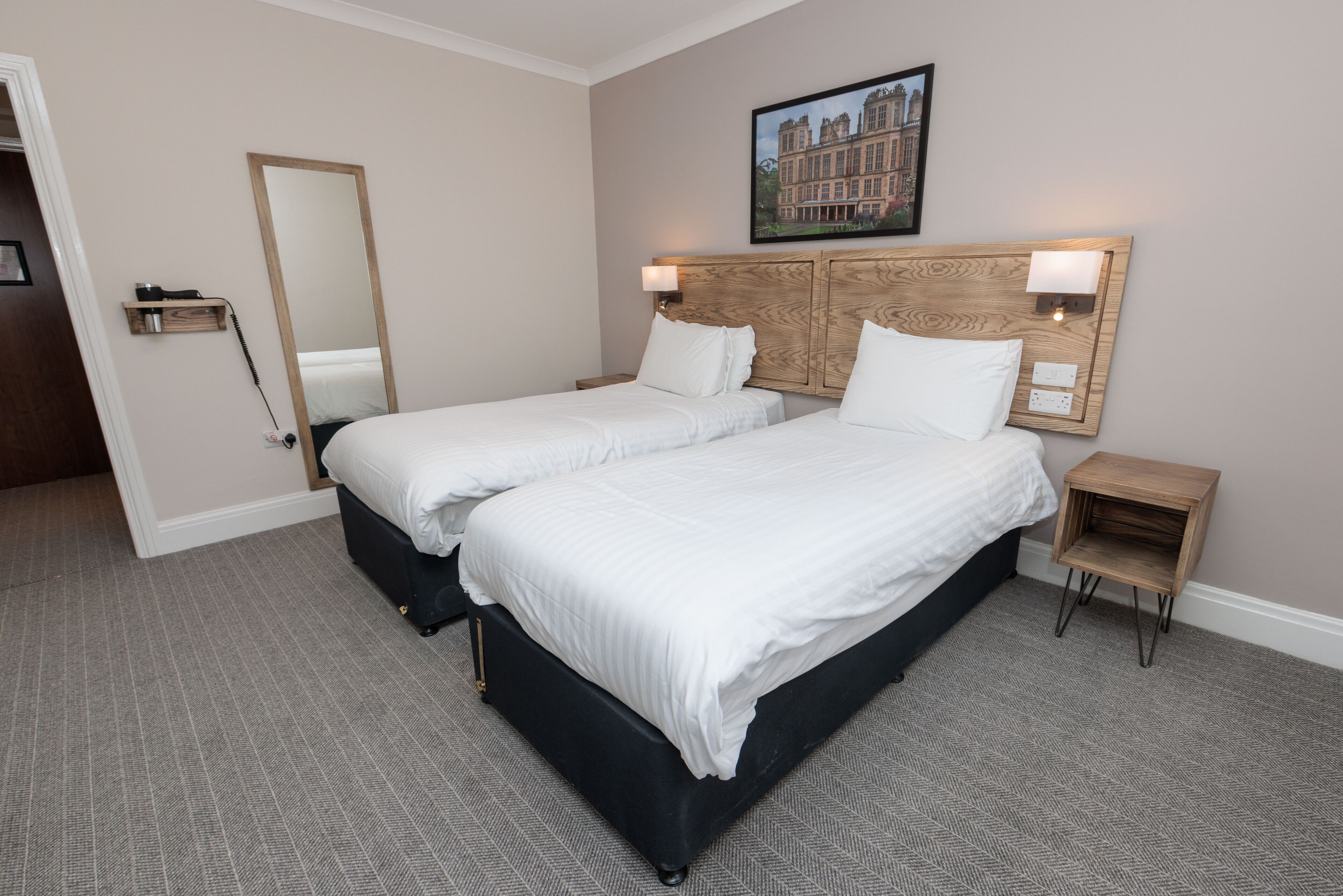 A hotel room with two beds, a large mirror, a headboard with built-in lighting, and a framed picture on the wall.