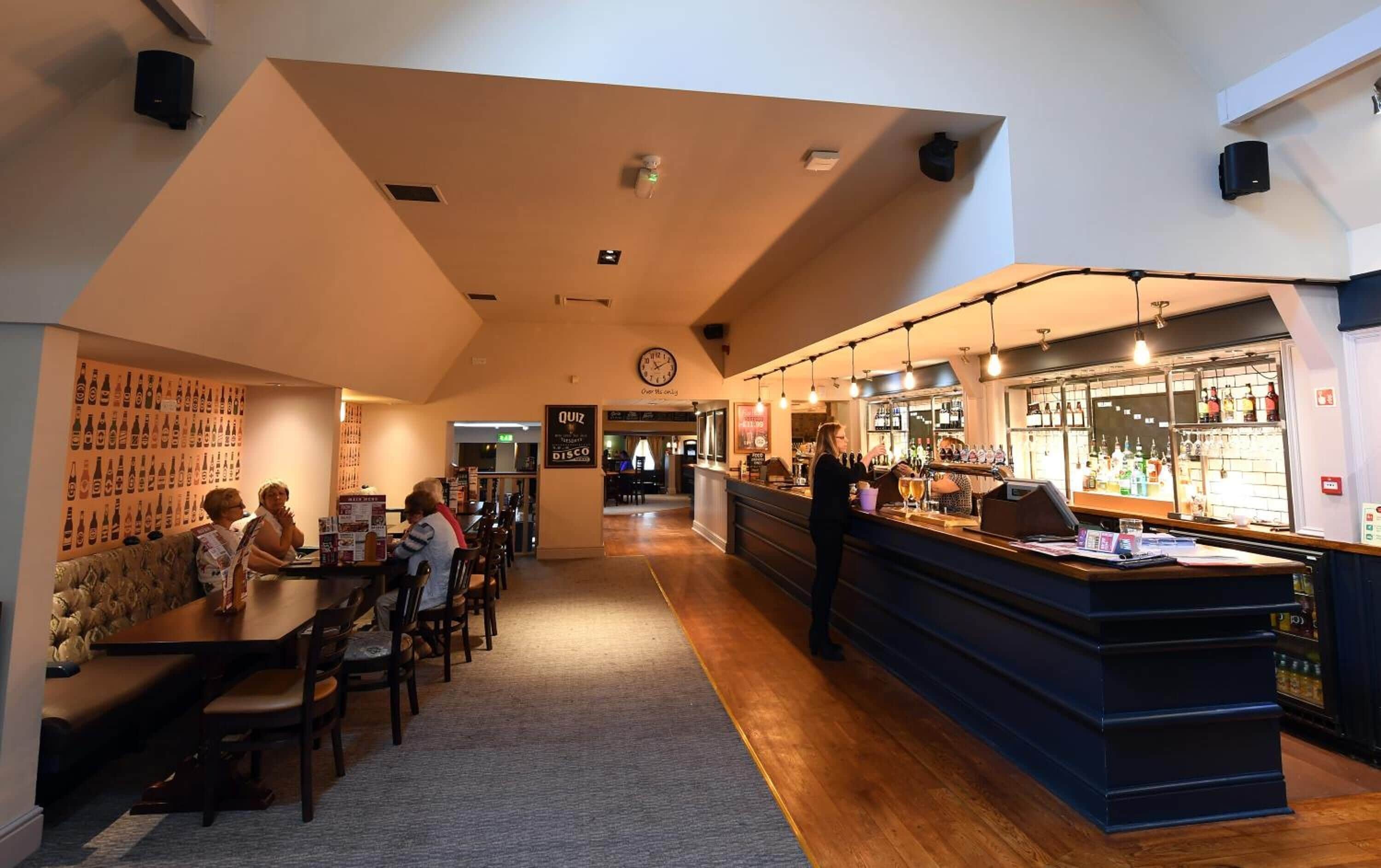 A restaurant with a bar area, wooden tables, and chairs.