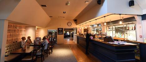 A restaurant with a bar area, wooden tables, and chairs.