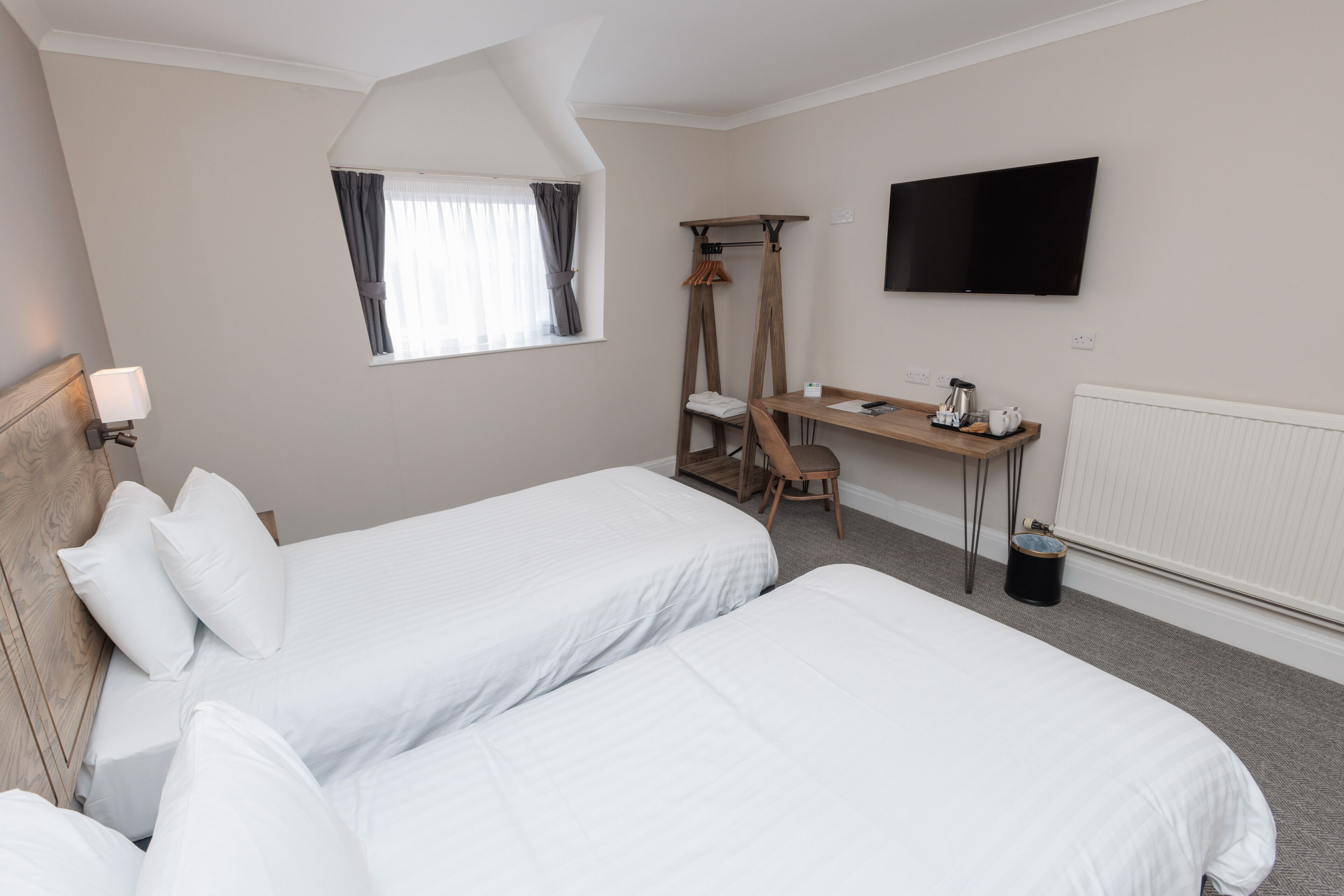 A hotel room with two beds, a desk, a chair, a TV, and a window with curtains.