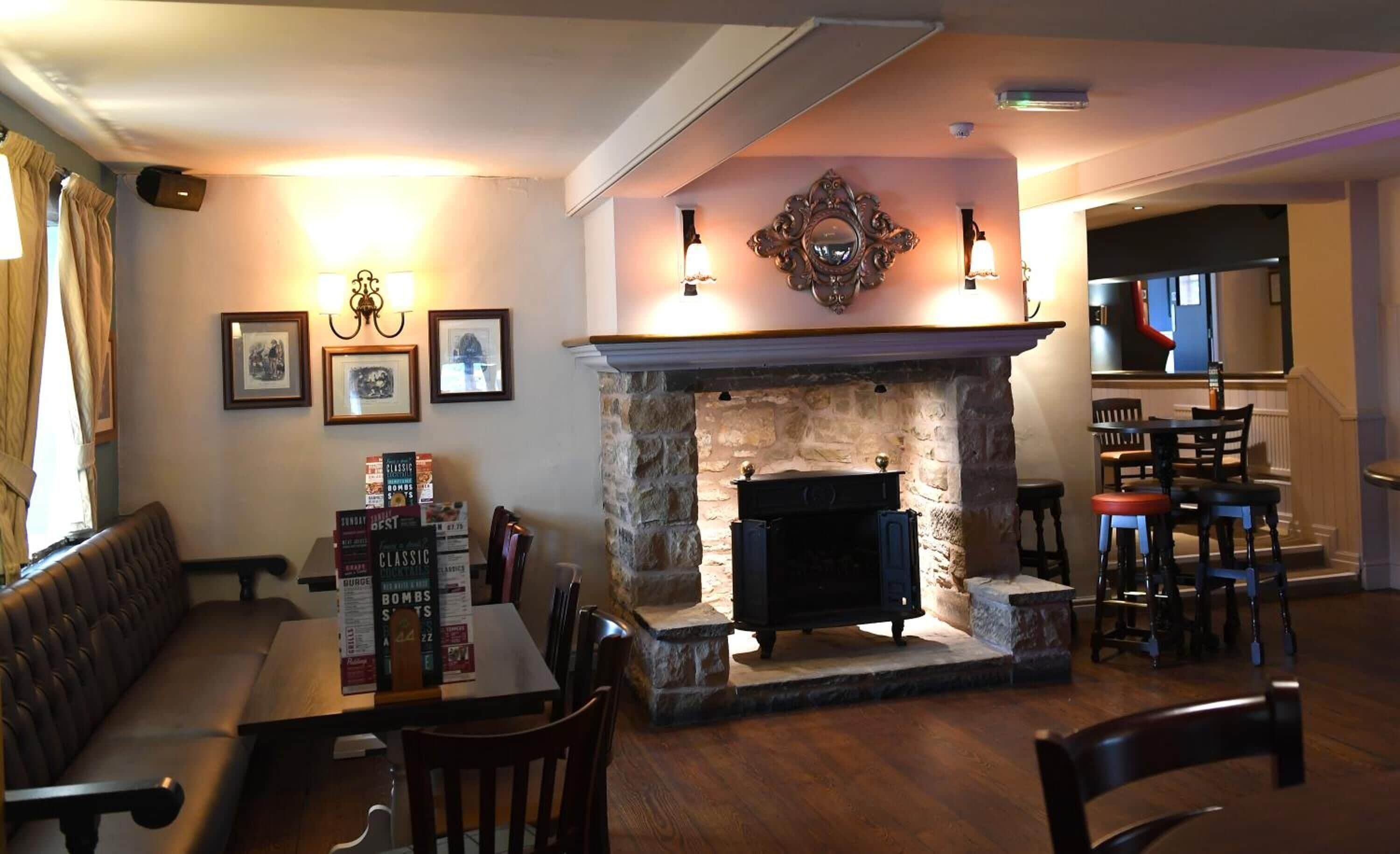 A cozy lounge area with a stone fireplace, framed pictures on the wall, and a bar area with stools.