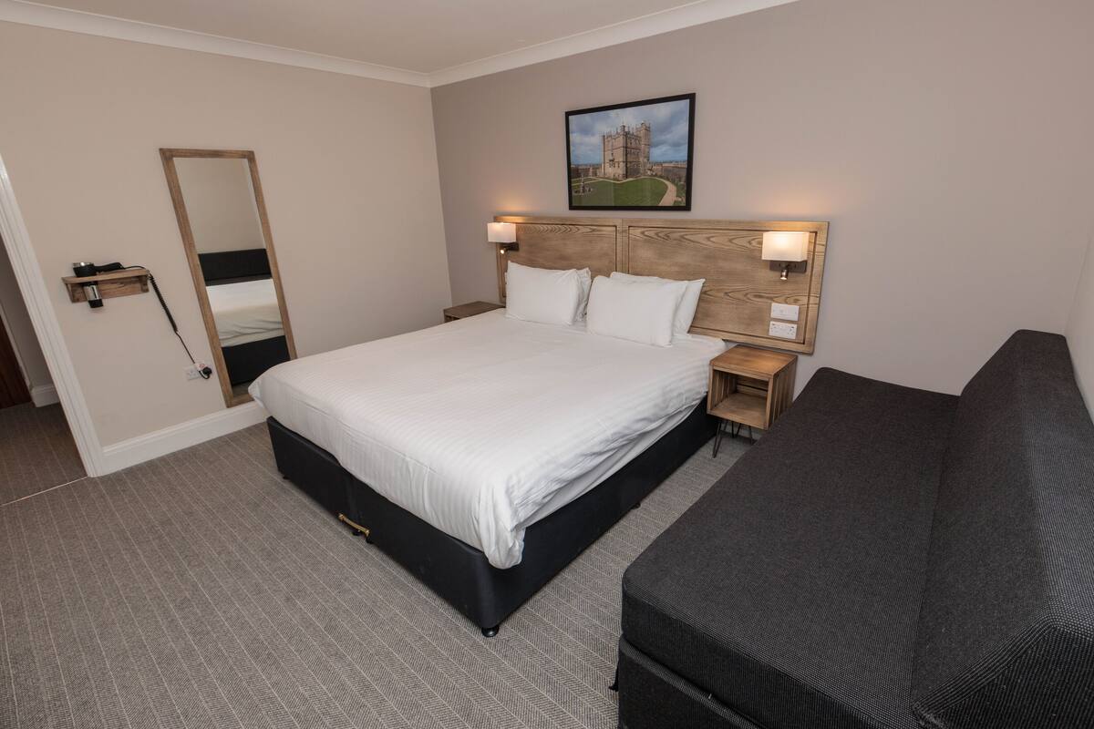 Una camera d'albergo con un letto grande, comodini con lampade, uno specchio e un quadro appeso al muro.