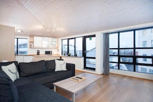 A modern living room with a grey sofa, a wooden coffee table, and a view of the city through large windows.
