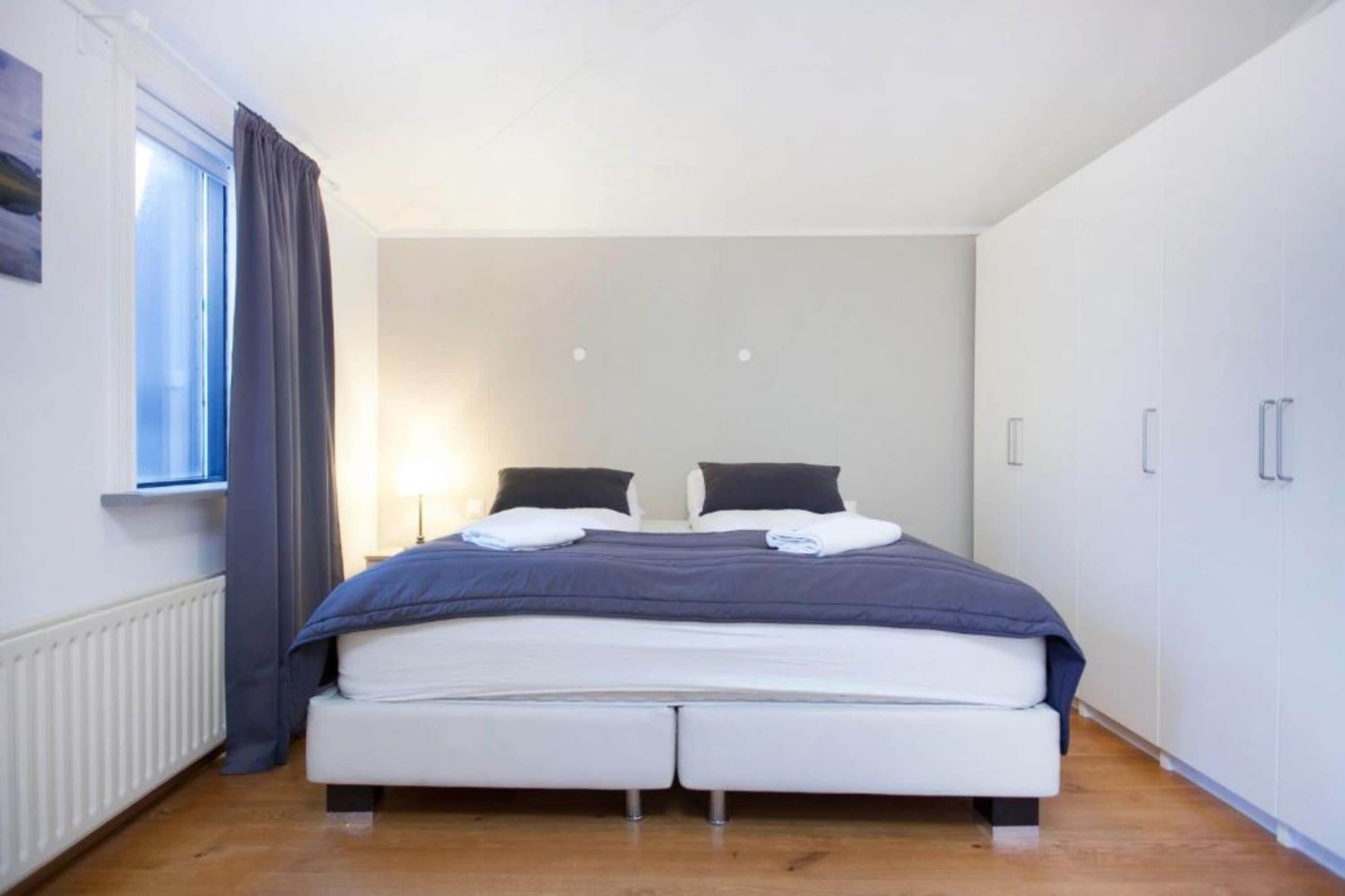 Un dormitorio con cama, dos mesitas de noche, una ventana con cortinas y un radiador.