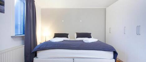Un dormitorio con cama, dos mesitas de noche, una ventana con cortinas y un radiador.