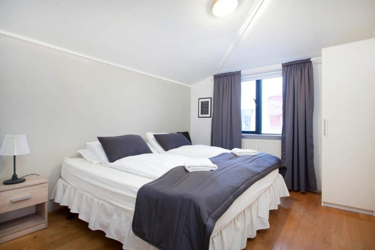 Ein Schlafzimmer mit zwei Betten, einem Nachttisch, einem Fenster mit Vorhängen und einer Heizung.