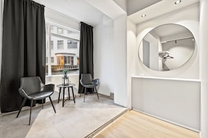 A modern room with a large window, two black chairs, a small table with a plant, and a round mirror on the wall.