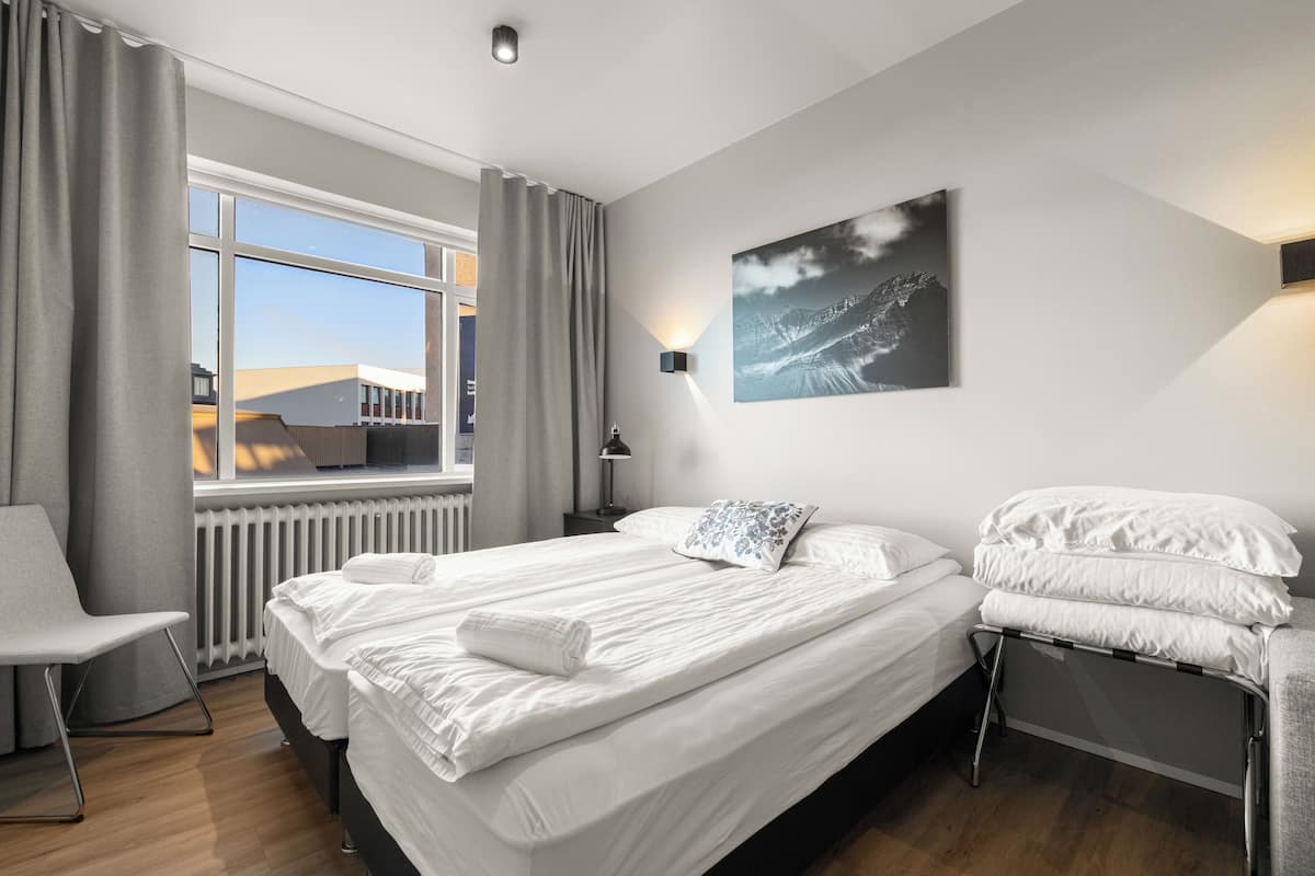 Ein modernes Hotelzimmer mit einem großen Bett, einem Sessel, einem Schreibtisch und einem Fenster mit Vorhängen.