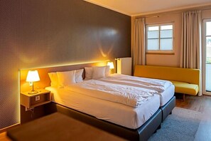 A hotel room with a large bed, bedside tables, a bench, and a window with curtains. - Hotel Seeblick (Friesoythe)