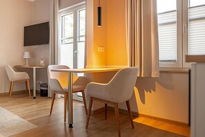 A modern room with a dining table, two chairs, a TV mounted on the wall, and a window with blinds.