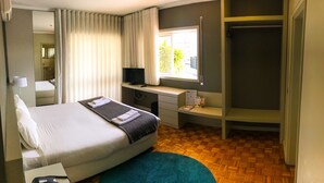 Habitación de hotel con cama, escritorio, televisión y ventana con vista a palmeras.