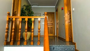 Una escalera de madera con barandilla, una planta en maceta y una puerta con un número.
