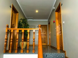 Una escalera de madera con barandilla, una planta en maceta y una puerta con un número.