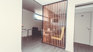 Una habitación con un separador de madera, una zona de comedor con sillas y una mesa, y una puerta con una 'S'.
