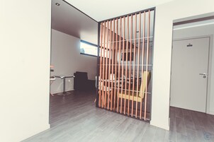 Una habitación con un separador de madera, una zona de comedor con sillas y una mesa, y una puerta con una 'S'.