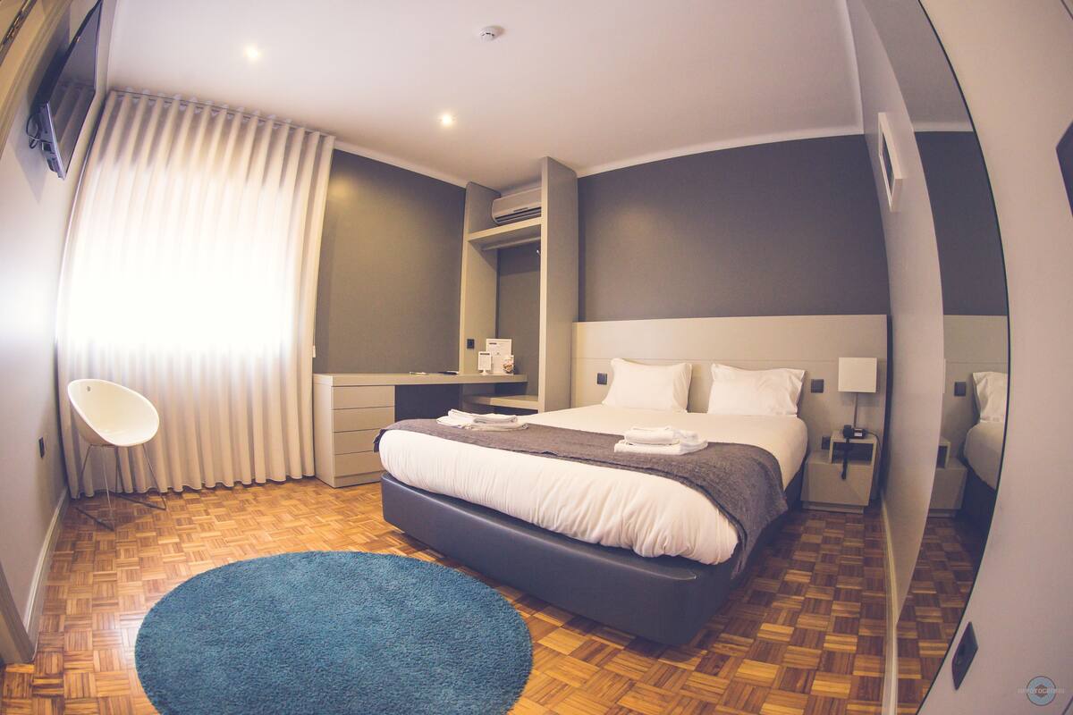 Quarto de hotel moderno com uma cama grande, mesas de cabeceira, escrivaninha e uma cadeira.