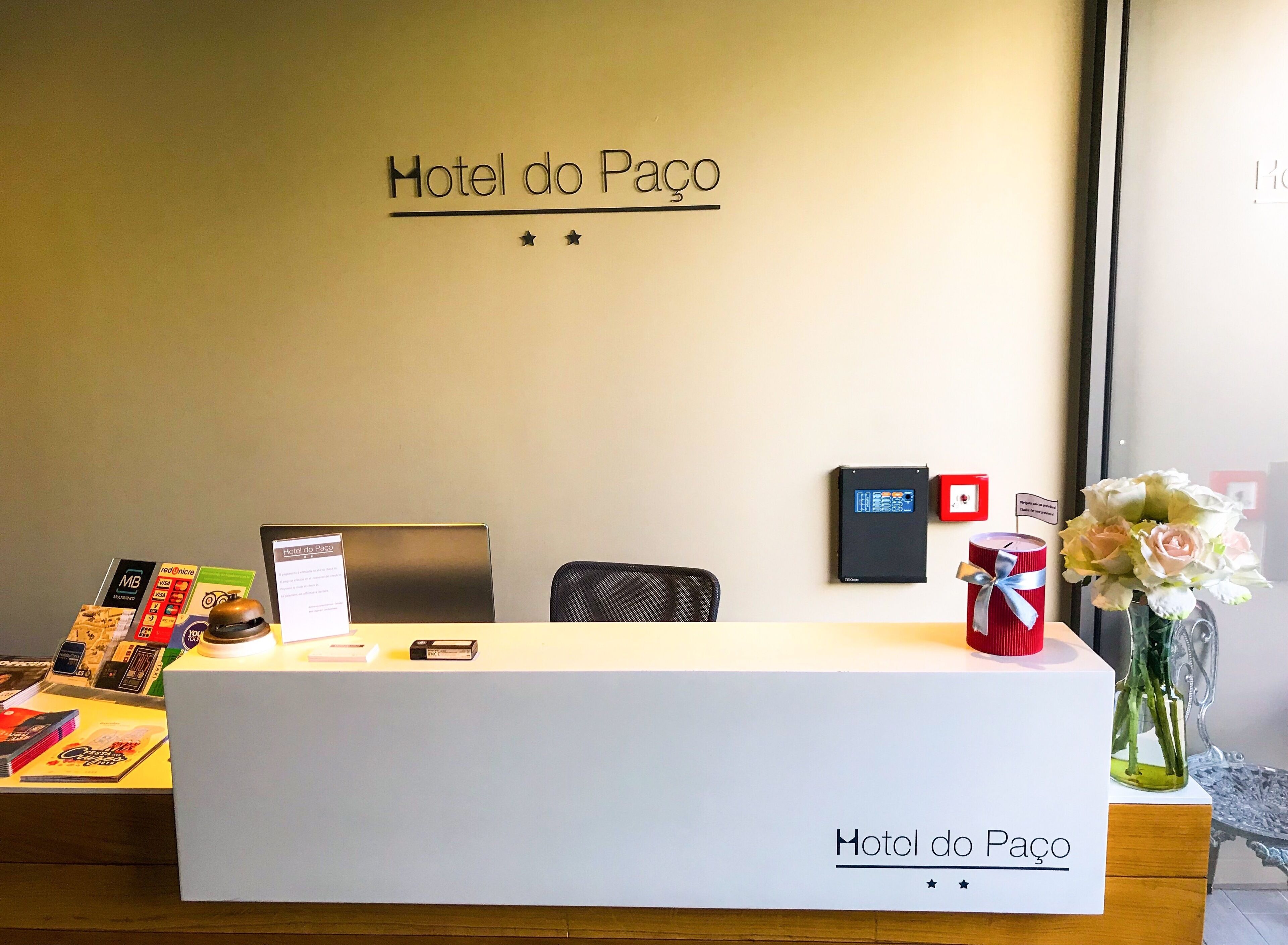 Un comptoir d’accueil d’hôtel avec une enseigne indiquant « Hotel do Paço » et un écran numérique.