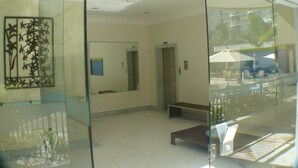 A modern lobby with a glass partition, an elevator, and a seating area with umbrellas. - Barra Dolce Vita Residence Service (Rio de Janeiro)