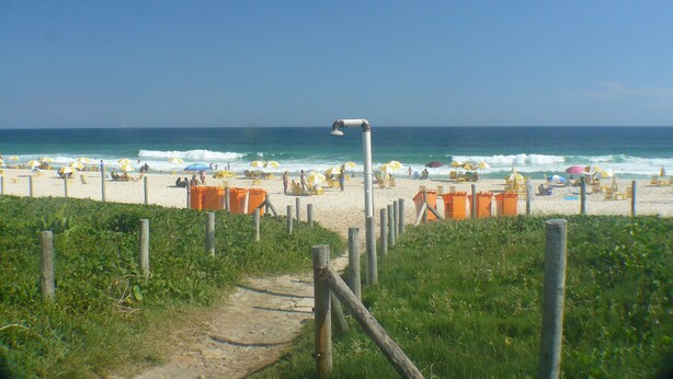 A beach with a path leading to the sea, surrounded by umbrellas and beach chairs. - Barra Dolce Vita Residence Service (Rio de Janeiro)