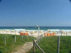 Una playa con un sendero que lleva al mar, rodeada de sombrillas y sillas.
