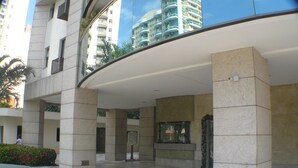 A modern hotel entrance with a curved roof, large pillars, and a tiled floor. - Barra Dolce Vita Residence Service (Rio de Janeiro)