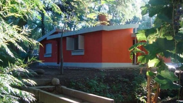 Ein rotes Gebäude mit einer kleinen Veranda und Stufen, die davor hochführen, umgeben von viel Grün.