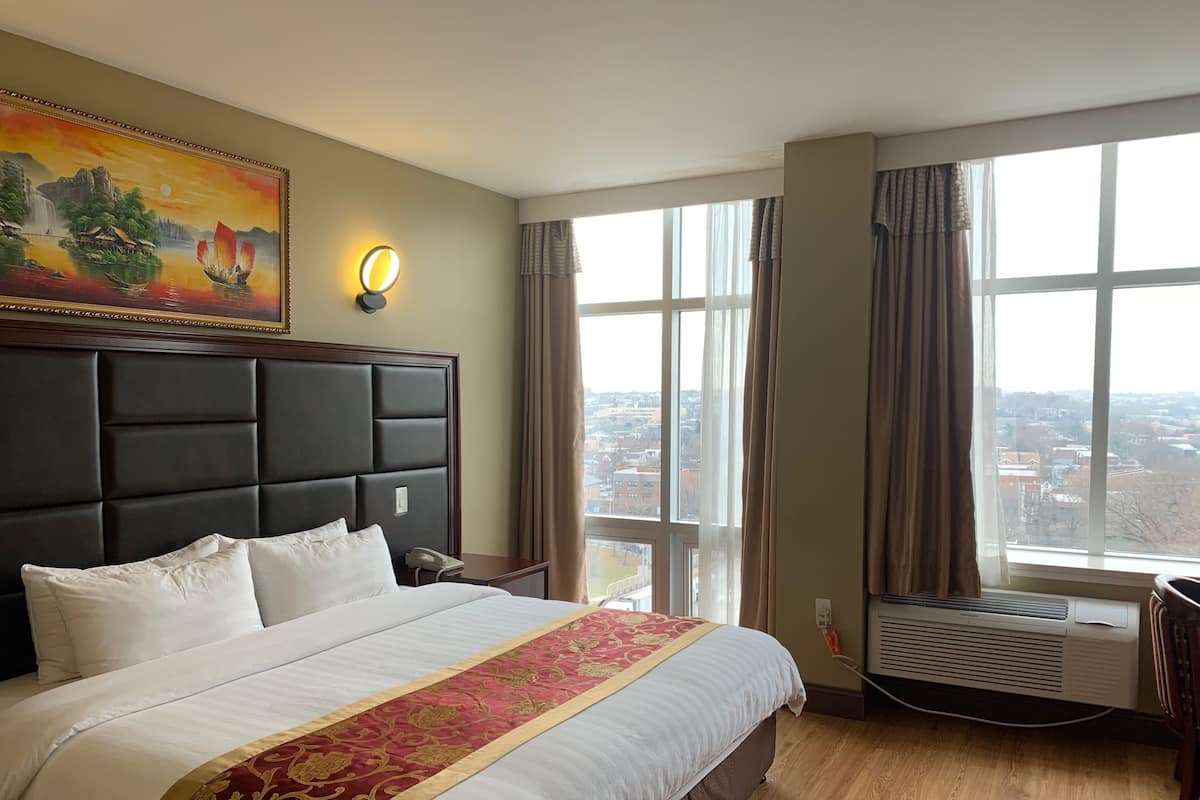 Habitación de hotel con una cama grande, cabecera, un cuadro, lámpara de noche, ventana con cortinas y un equipo de aire acondicionado.