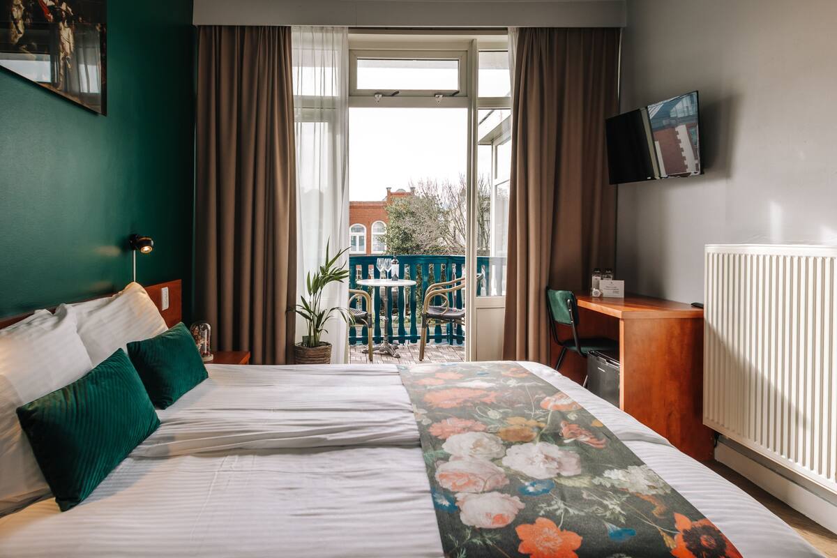 Ein Hotelzimmer mit Bett, Schreibtisch, Stuhl, Zimmerpflanze und Blick ins Freie.