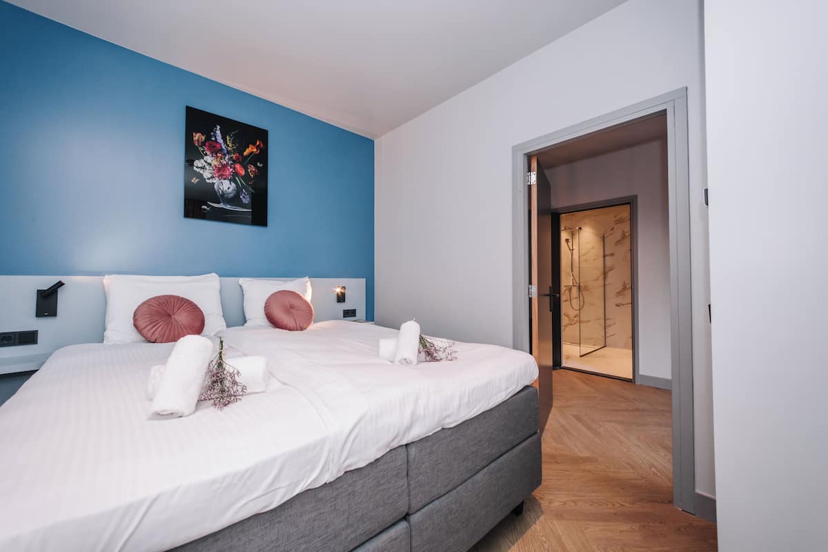 Ein modernes Schlafzimmer mit einem großen Bett, einer blauen Akzentwand und einer Holztür, die ins Badezimmer führt.