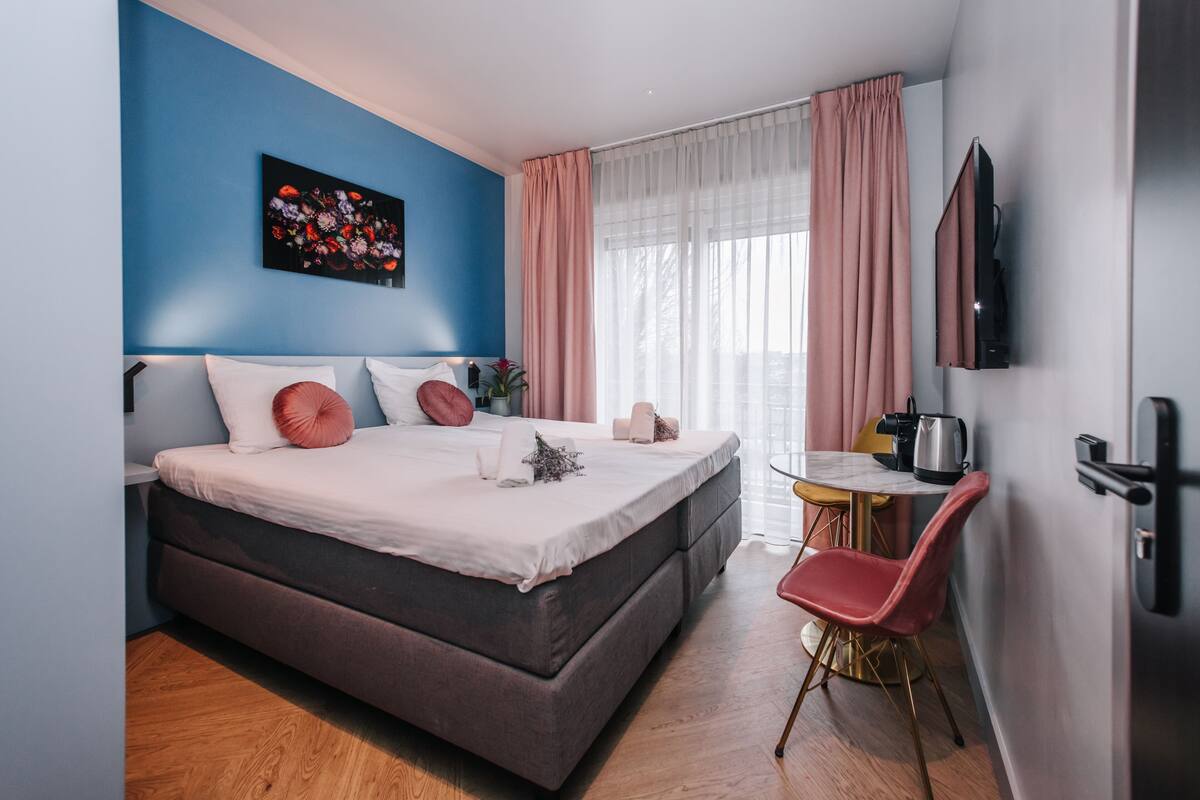 Ein modernes Schlafzimmer mit einem großen Bett, einem kleinen Tisch, einem Stuhl und einem an der Wand befestigten Fernseher.