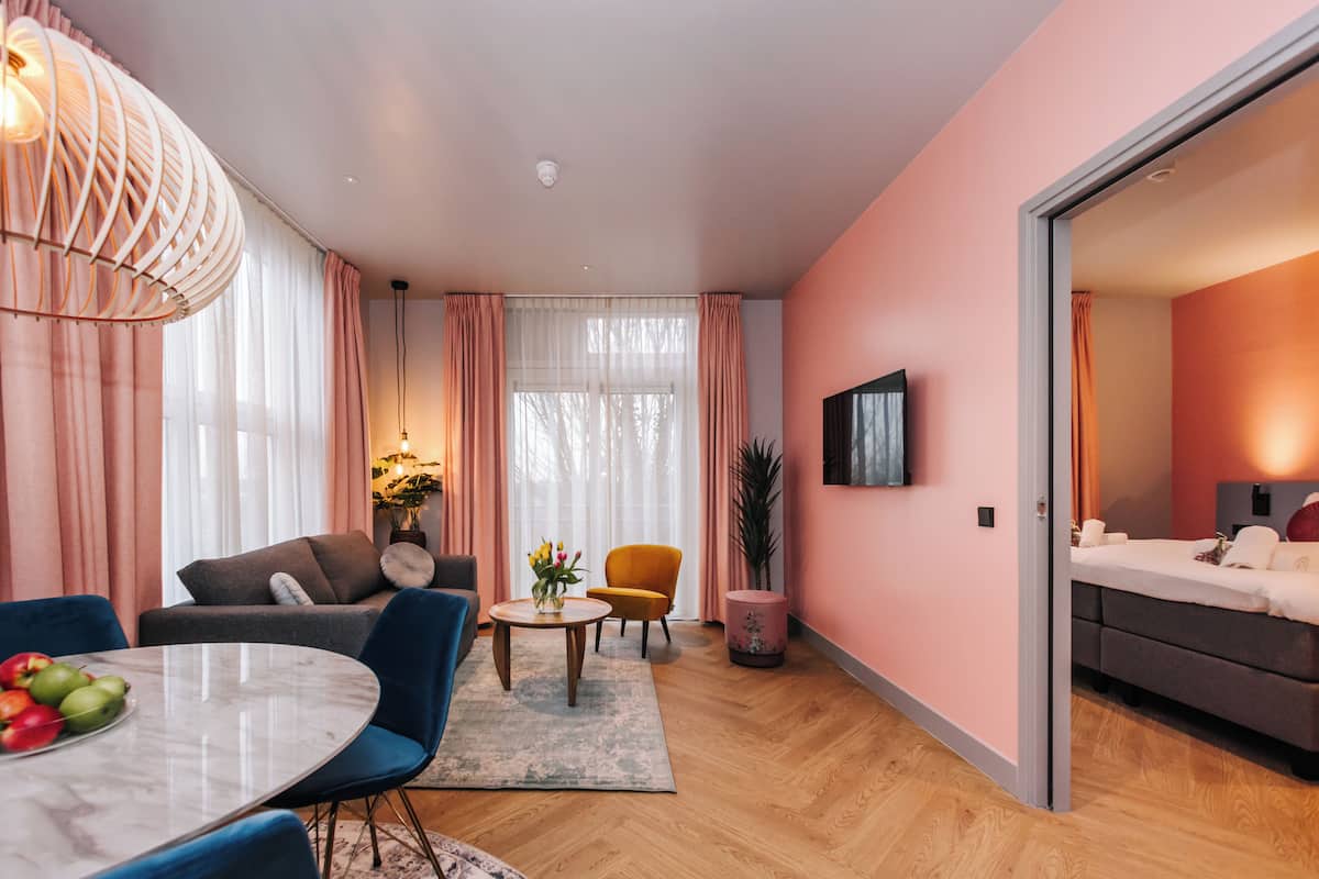 Ein modernes Wohnzimmer mit rundem Tisch, blauen Stühlen, einer Couch und einem an der Wand befestigten Fernseher.